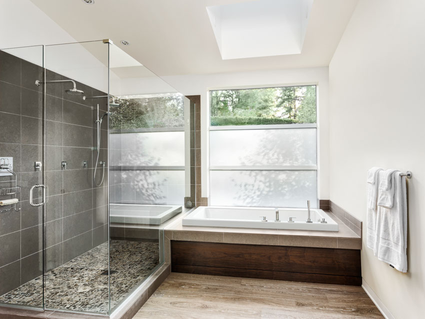 Ванная комната с ванной из стекловолокна, душевой, стеклянной дверью, окнами, деревянным полом и световым люком.