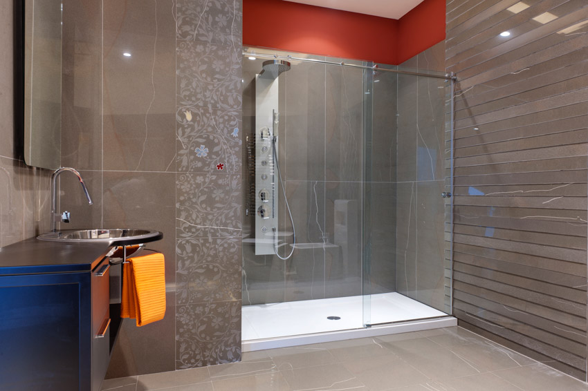 Ванная комната с современной умной насадкой для душа, стеклянной дверью, кафельным полом, зеркалом и раковиной.