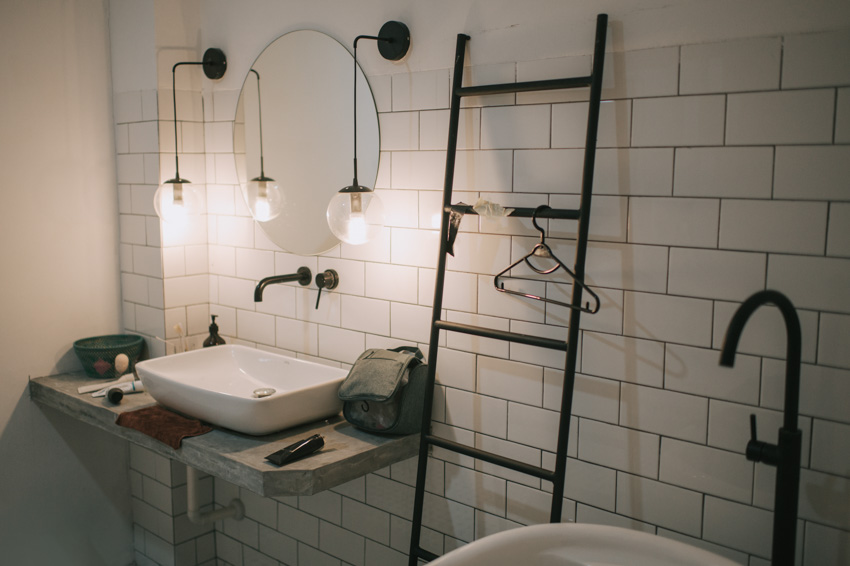 Ванная комната с белой плиточной стеной, раковиной, зеркалом и небольшими подвесными светильниками