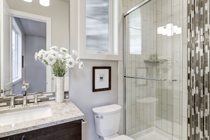 Ванная комната с душевой зоной, стеклянная дверь, плитка в стиле метро, ​​зеркало, туалет и столешница.