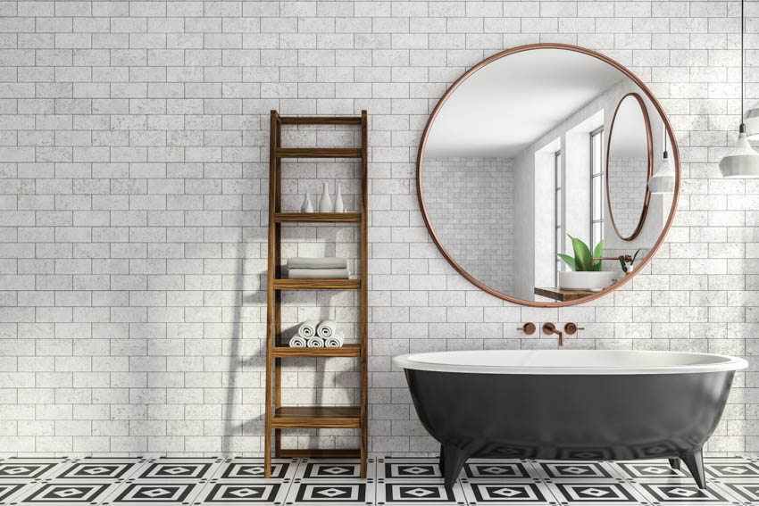 Ванная комната с серой плиткой, круглым зеркалом и черной ванной