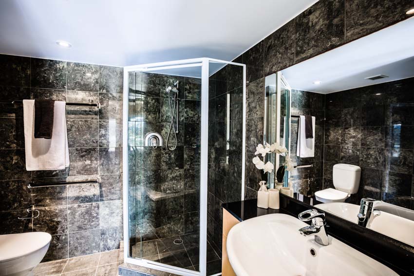 Ванная комната с ониксовой душевой стеной, зеркалом, раковиной, полотенцесушителем и унитазом.