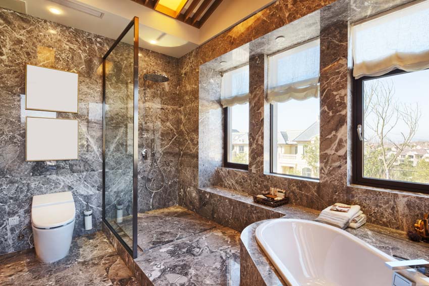 Просторная ванная комната со стенами из оникса, окнами, ванной, туалетом и стеклянной перегородкой