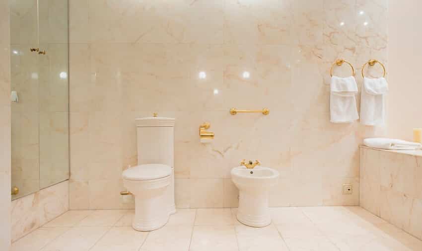 Интерьер туалета с мраморным полом и стенами, шкафом с зеркальными дверями и полотенцами, висящими на латунном кольце для полотенец