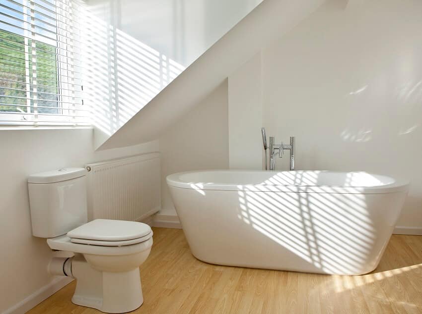 Современная ванная комната с отдельно стоящей ванной, туалетом с деревянным полом и окнами с жалюзи.