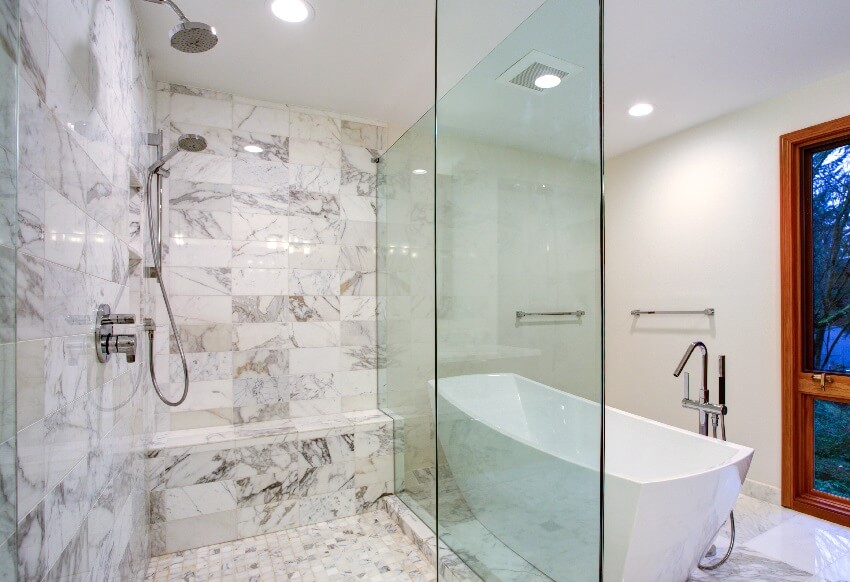 Элегантная ванная комната с отдельно стоящей ванной в сочетании с установленным на полу смесителем на мраморном полу перед стеклянной душевой кабиной с тропическим душем и обрамлением из серого мрамора.