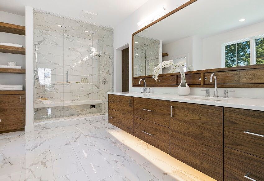 Современная ванная комната середины века с большими зеркальными мраморными плитками на стенах и полах, деревянными шкафами и полками, а также душевая со скамейкой.