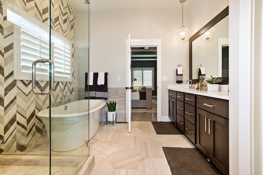Ванная комната с отдельно стоящей ванной, душем, коричневыми шкафчиками, декоративными растениями, косметическим зеркалом и кафельным полом.