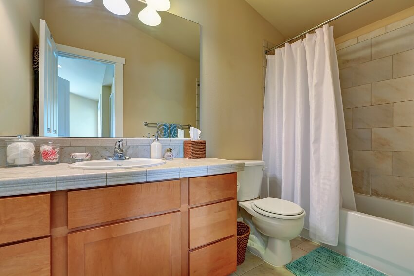 Современный туалетный столик в ванной комнате с выдвижными ящиками и мраморной столешницей, полной ванной, душем с белой занавеской и туалетом.