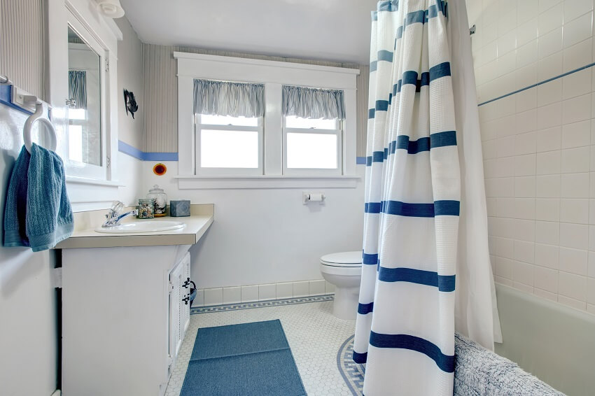 Белая ванная комната с белым ковриком для умывальника, синим ковриком и полосатыми занавесками