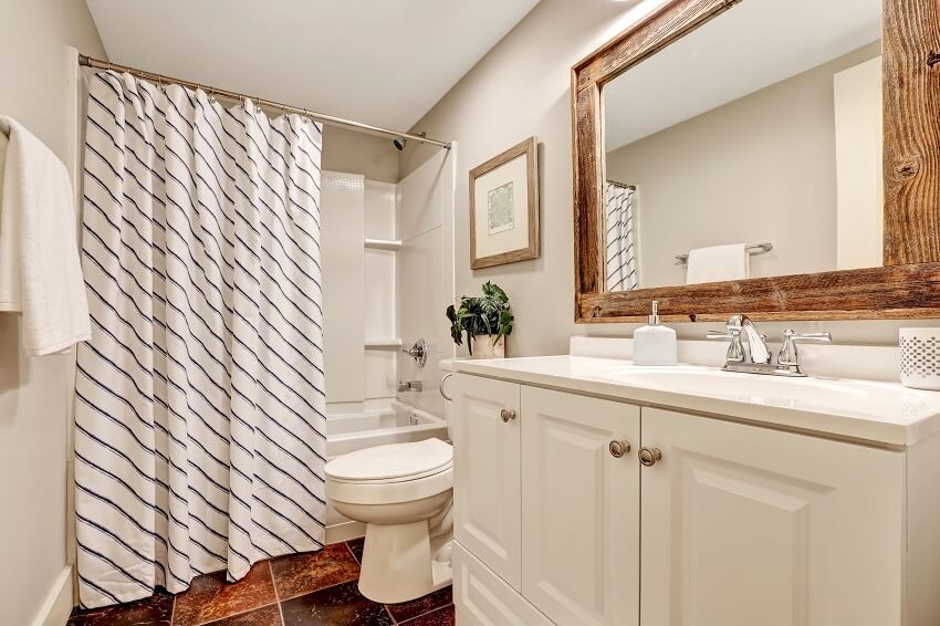 Ванная комната в белых тонах с туалетным столиком и зеркалом в деревянной раме, украшенным цветочным горшком и полосатой занавеской