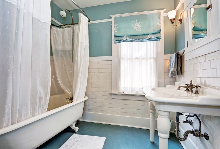 Голубой интерьер ванной комнаты с белой плиткой, отделкой стен, белой раковиной и ванной