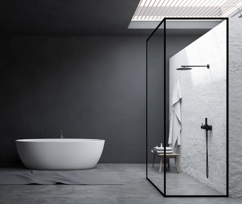 Интерьер стильной ванной комнаты с серыми и белыми лепными стенами, душевой кабиной с бетонным полом, стеклянными стенами, белой ванной и столом