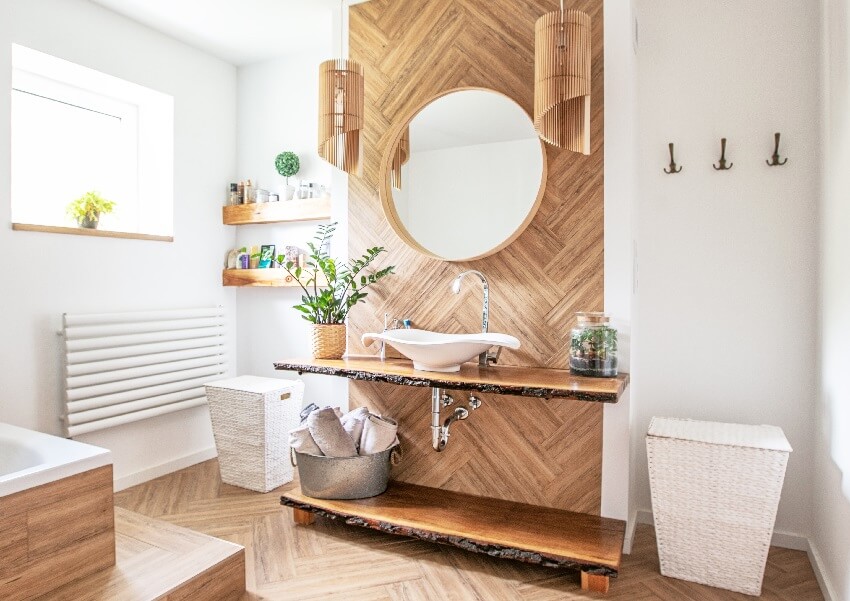 Белая раковина на деревянной стойке с подвесным круглым зеркалом в интерьере ванной комнаты