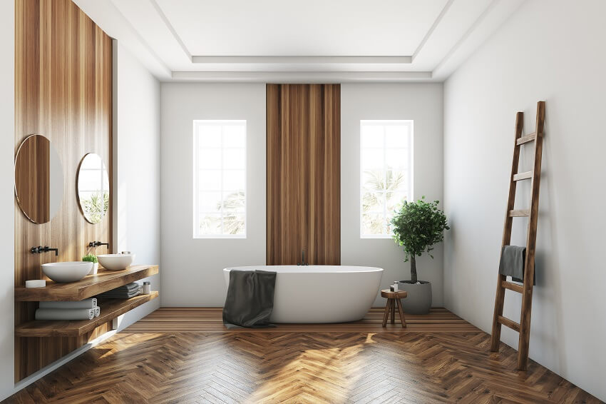 Белый и деревянный интерьер ванной комнаты с виниловыми обоями, деревянным полом, белой ванной и двумя узкими окнами 