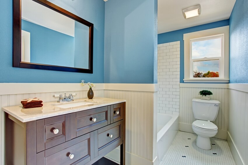 Интерьер ванной комнаты с синей стеной и белой панелью, ванна с отделкой плиткой и коричневой тумбой с зеркалом