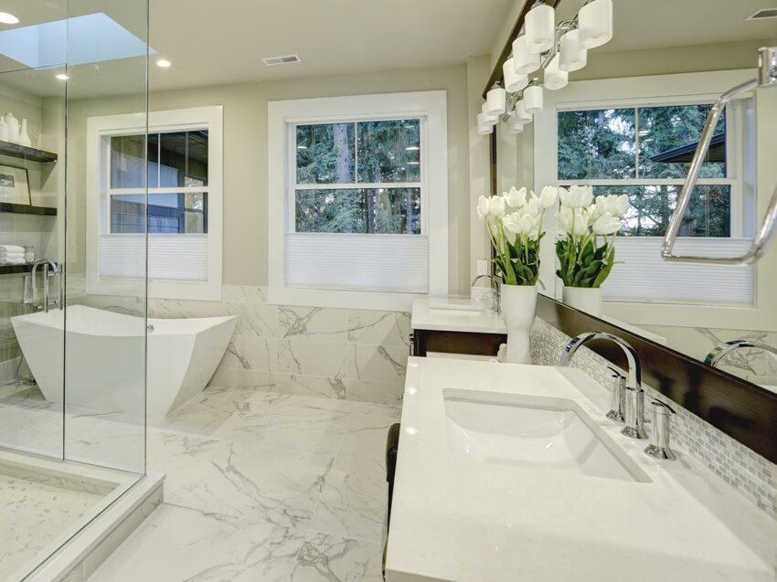 Удивительная главная ванная комната из белого и серого мрамора с большой стеклянной душевой кабиной, отдельно стоящей ванной и световыми люками на потолке.