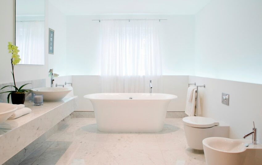 Светлая, просторная и элегантная ванная комната с раковиной, унитазом, отдельно стоящей ванной и стенами, наполовину выложенными плиткой.