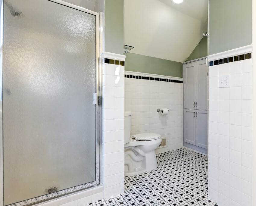 Половина стен ванной комнаты выложена плиткой метро с черной плиткой поверх винтажного черно-белого кафельного пола.