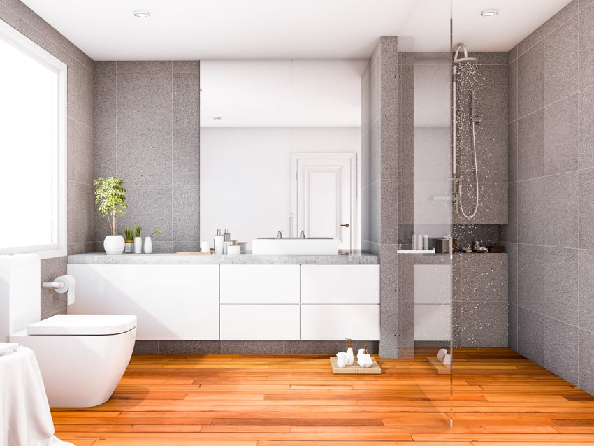 Ванная комната с серыми стенами, деревянным полом, белыми шкафами, зеркальным туалетом