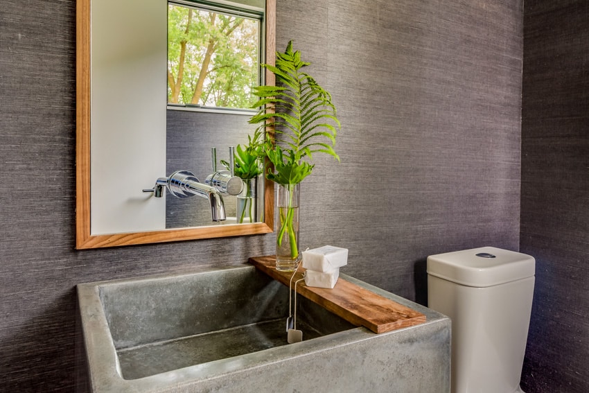 Бетонно-серая раковина и настенное зеркало в ванной комнате с растениями