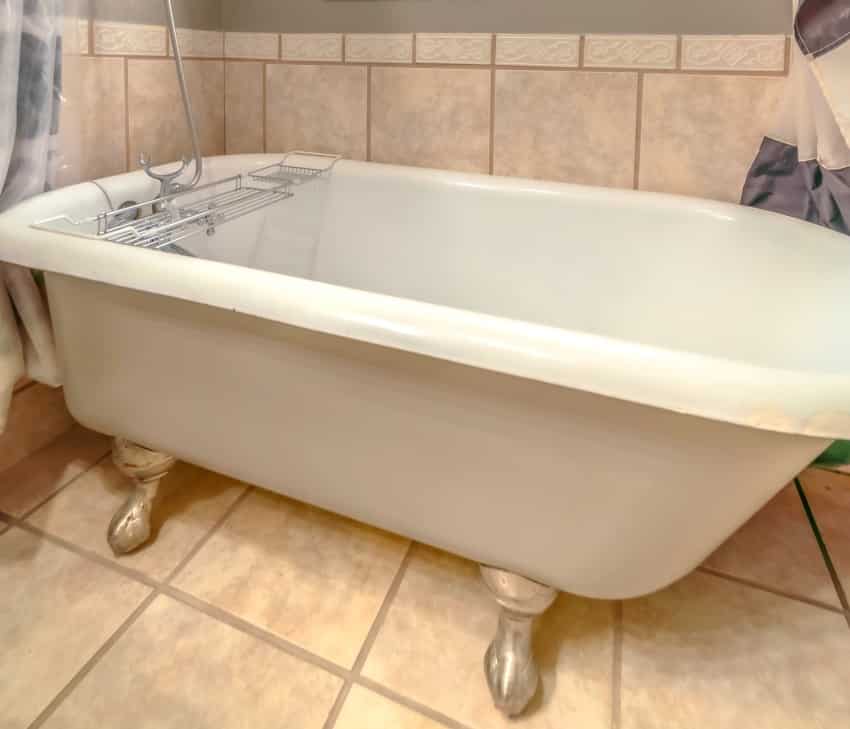 ванна с некоторыми отслоениями на углу и душ в ванной комнате с плиткой на стене и полу