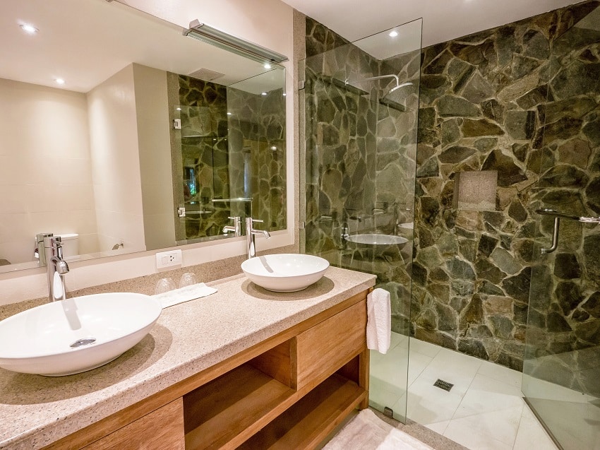 современная ванная комната с двумя круглыми белыми раковинами на гранитной столешнице из натурального камня и стеклянной душевой кабиной
