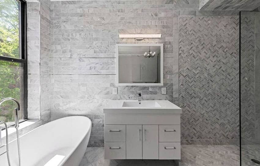 Современная ванная комната с мраморными плиточными стенами с одной раковиной и отдельно стоящей ванной.