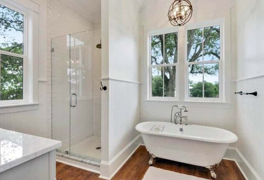 Традиционная ванная комната с небольшой душевой кабиной, деревянным полом, деревянными панелями и ванной на ножках