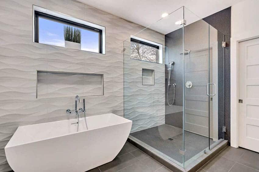 Modern bathroom with glass walk in shower and wavy contoured wall tile with freestanding tub