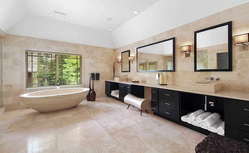 Современная главная ванная комната с ванной из травертина и умывальником темного цвета