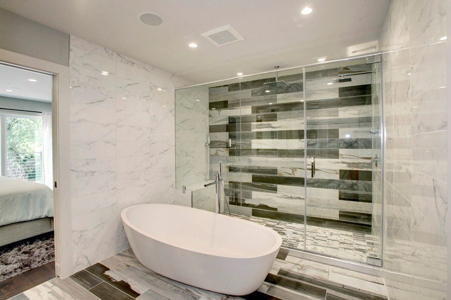 Современная главная ванная комната с большой ванной, мраморной плиткой на стене и фарфоровой душевой кабиной.