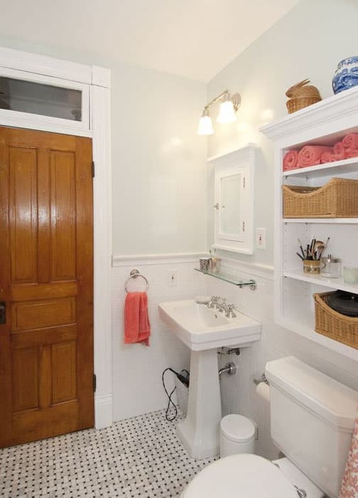 Уютная ванная комната со стеклянной полкой белого настенного шкафа и раковиной на пьедестале