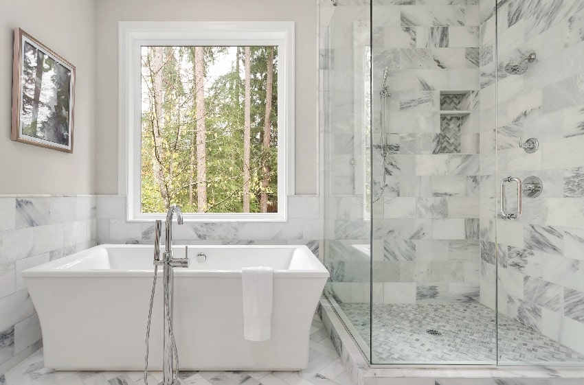 интерьер ванной комнаты с большой душевой кабиной элегантная плитка и глубокой ванной большое окно с видом на деревья