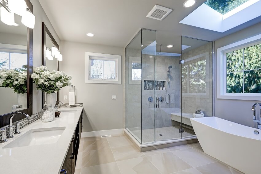 Просторная ванная комната в серых тонах с полом с подогревом, отдельно стоящей ванной, душевой кабиной, двойной раковиной и потолочными окнами.