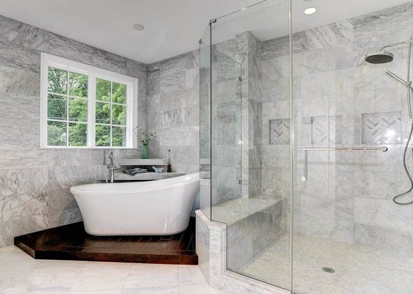 Основная ванная комната с тропическим душем, отделанным мраморной плиткой, и отдельно стоящей ванной на пьедестале.